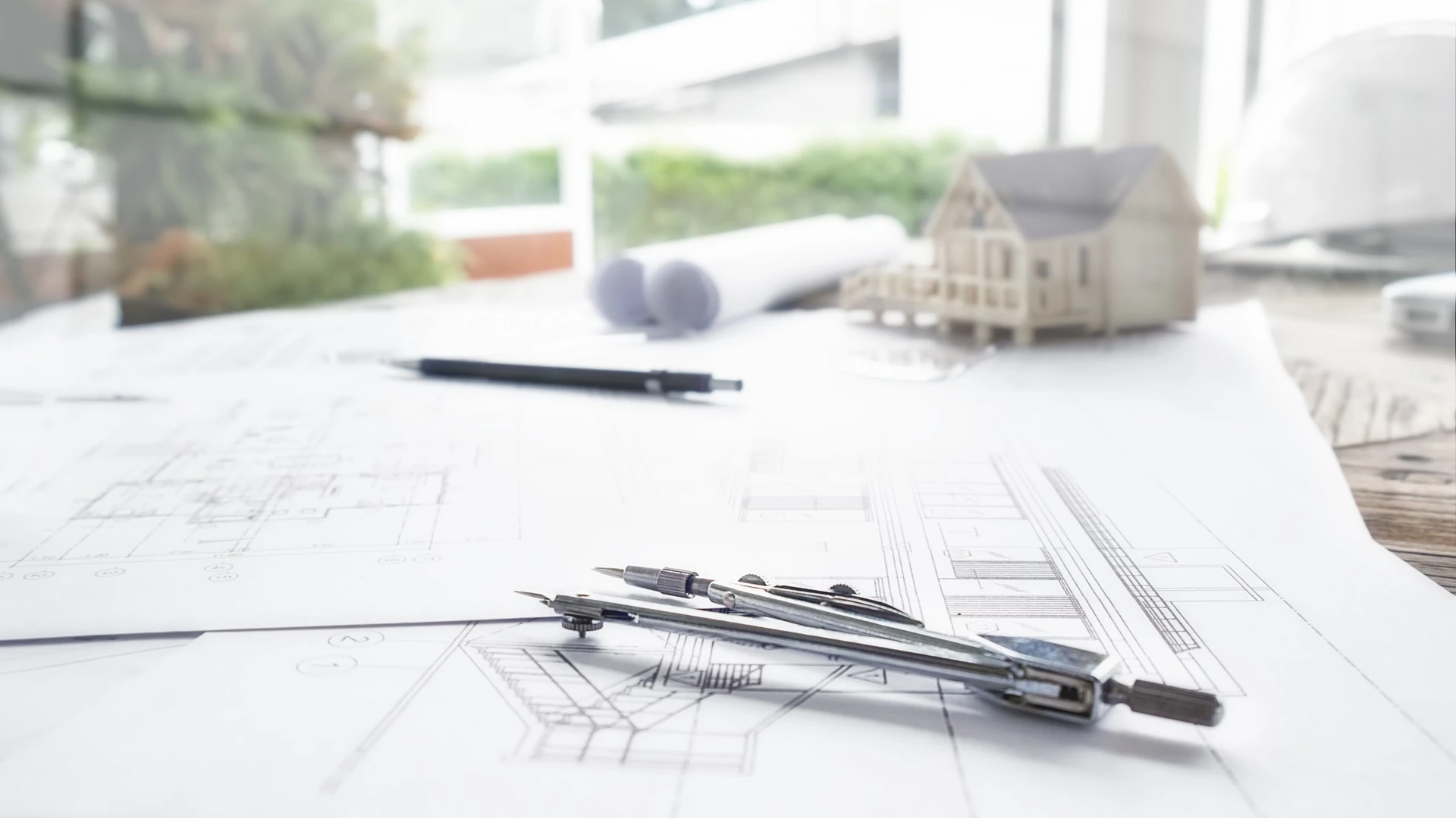 Gambar kerja desain arsitektur dengan jangka, pensil, dan maket rumah di meja perencana